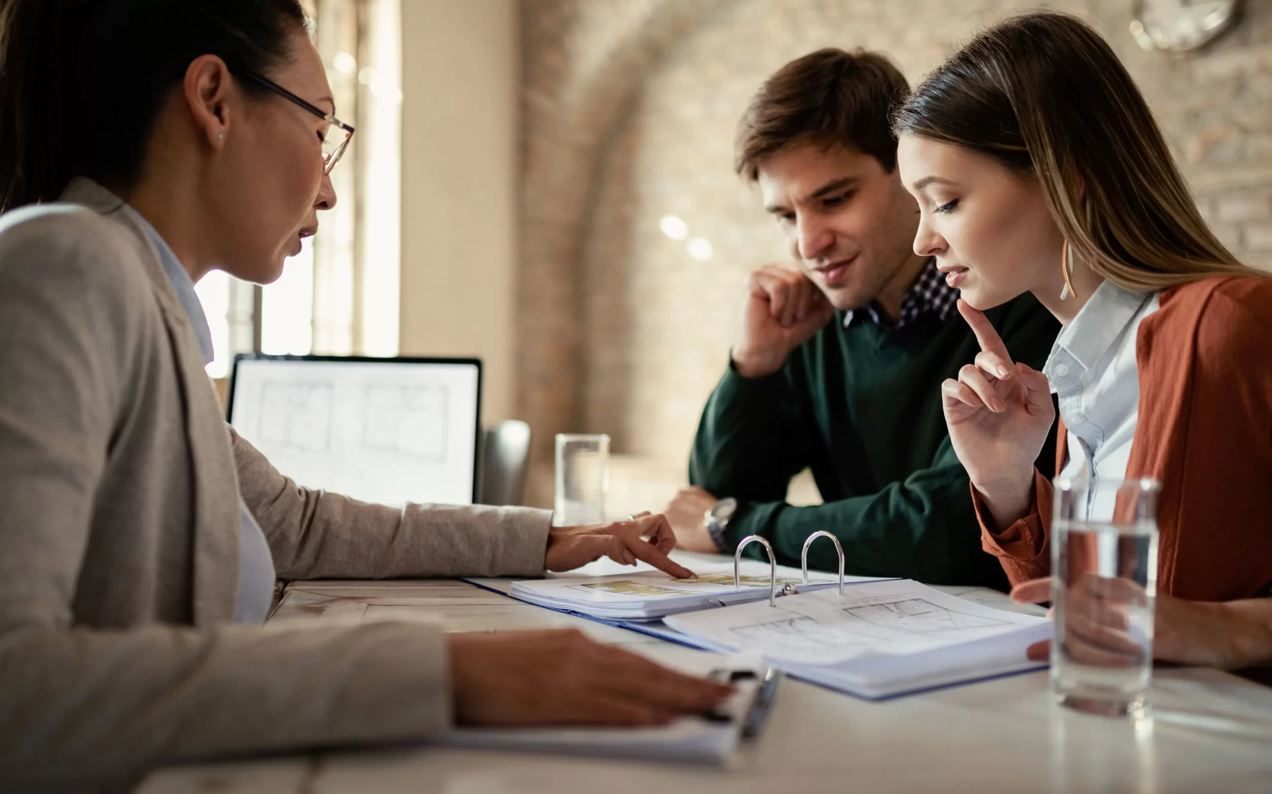 young-man-his-wife-examining-housing-plans-with-real-estate-agent-meeting-office